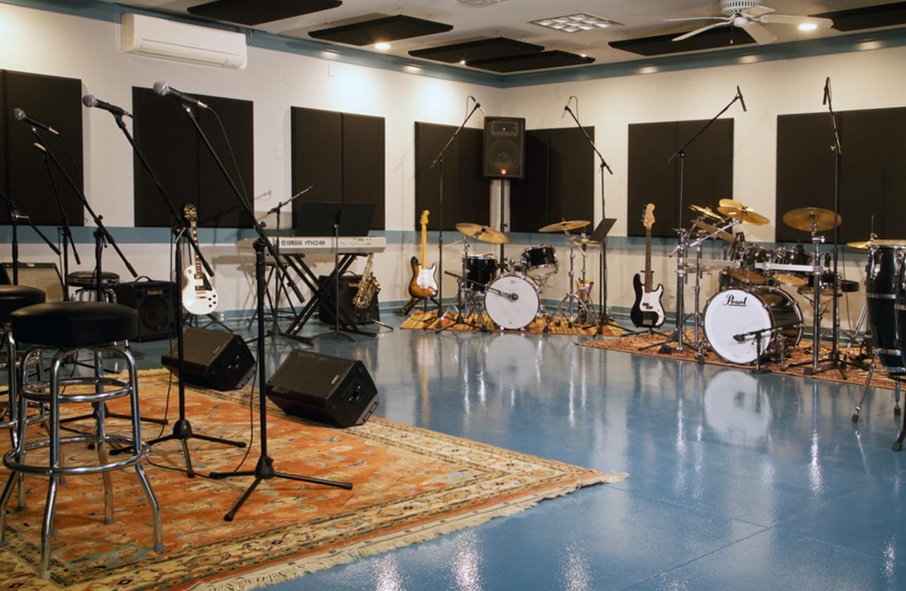 facilities2 The facilities at Borden Cottage include a music studio with various instruments such as drums, keyboards, guitars, microphones, and amplifiers, all arranged on a glossy blue floor and surrounded by soundproofing panels.